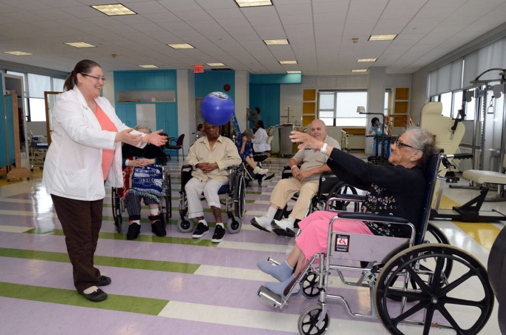 Therapist throws a weighted ball to a woman in a wheelchair in the therapy room